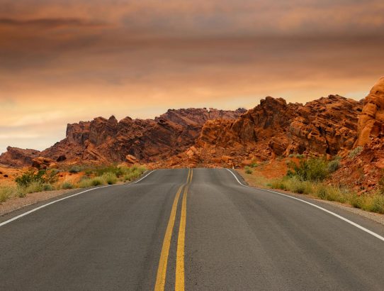 gray concrete road beside brown mountain during golden hour